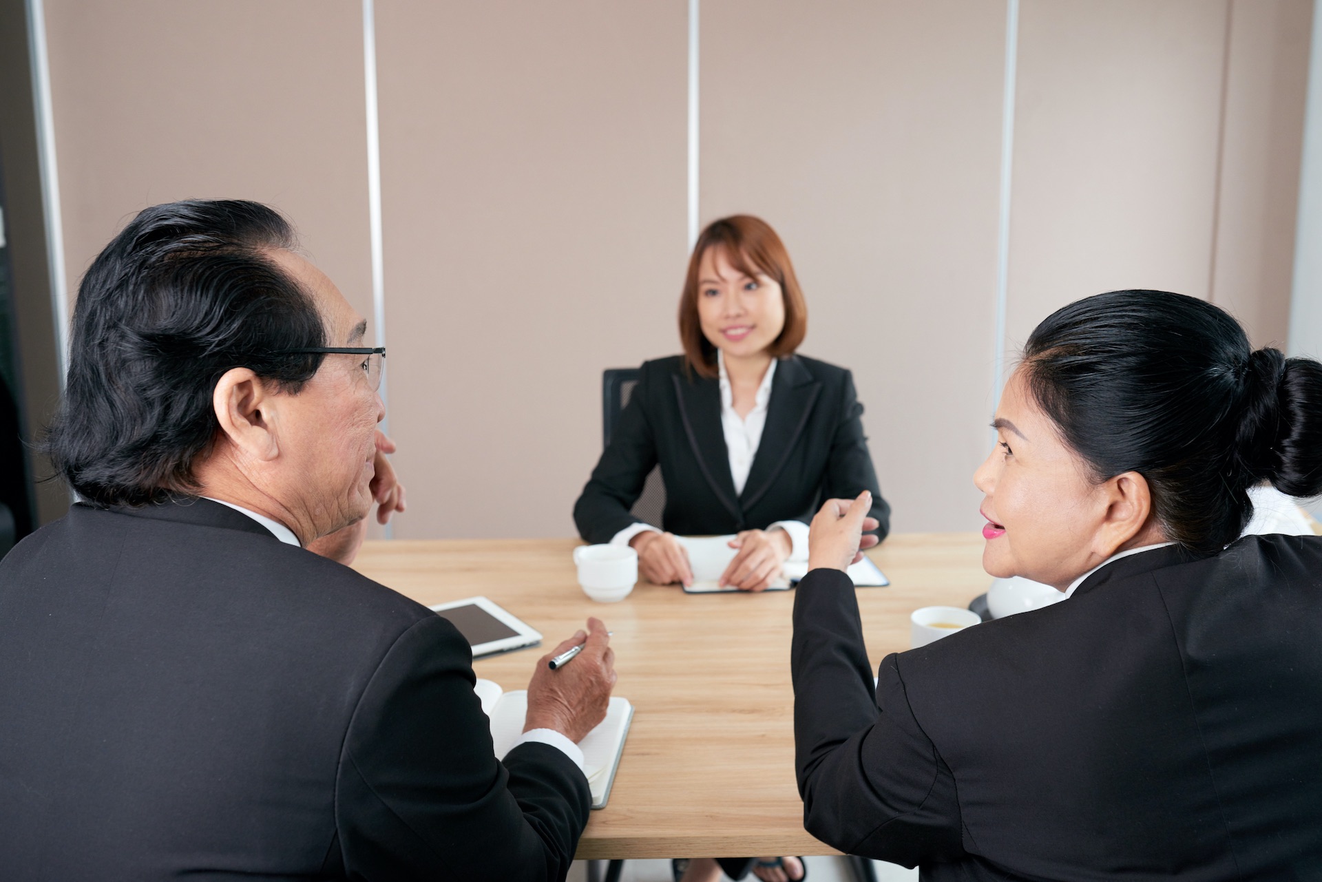 Zwei chinesische Businesspersonen, ein Mann und eine Frau, interviewen eine junge chinesische Frau bei einem Job-Vorstellungsgespräch