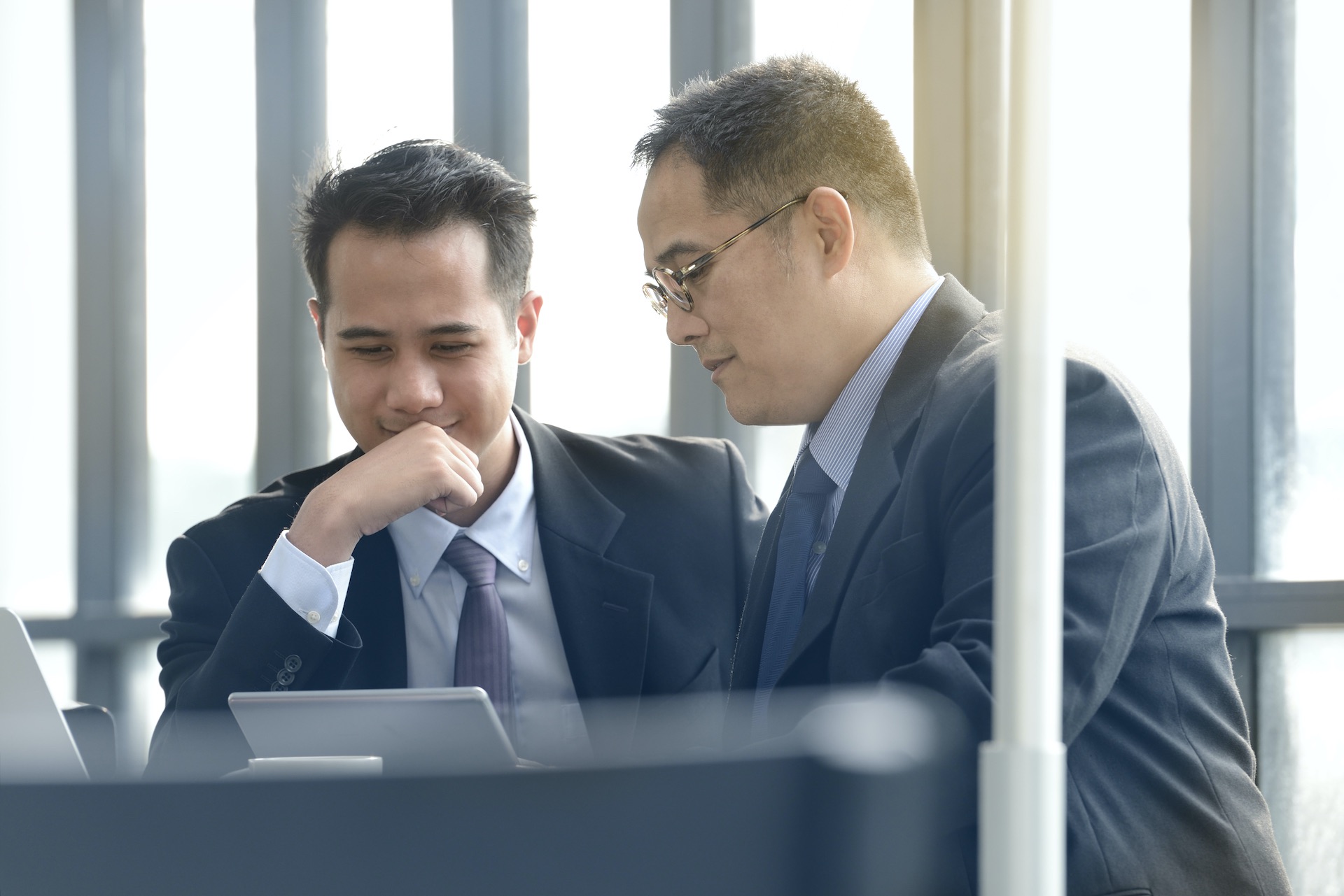 Zwei chinesische Business-Männer, die an einem iPad und Laptop zusammenarbeiten