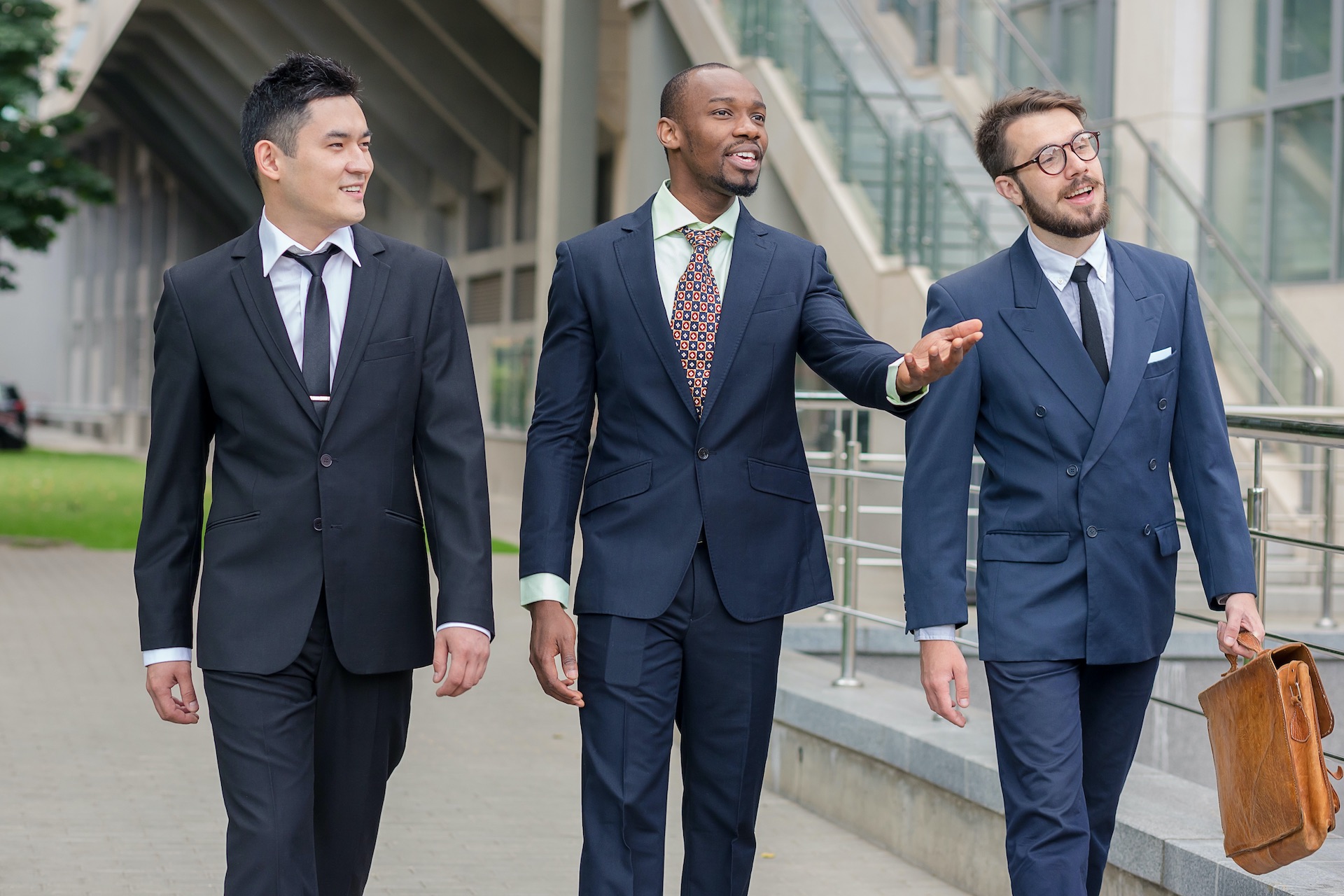 3 lächelnde Business Männer, chinesisch, afrikanisch und europäisch laufen von einem Gebäude weg